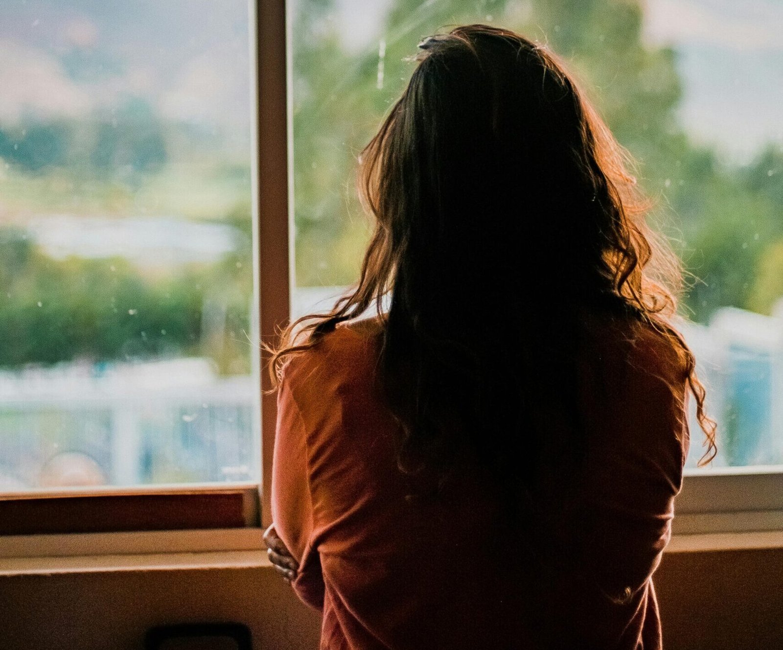 Mujer de espaldas viendo hacia la ventana, pensando, reflexionando.